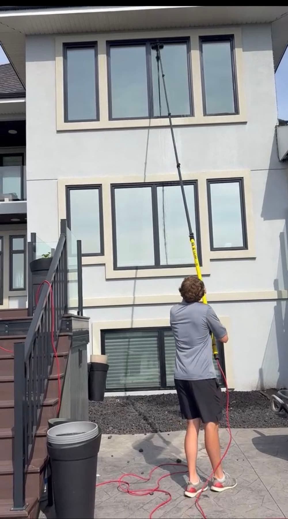 Person cleaning a high window with a pole cleaner outside a modern multi-story house.