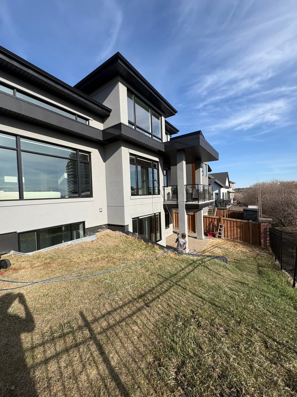 Modern two-story house with large windows and a balcony, set on a grassy hillside.