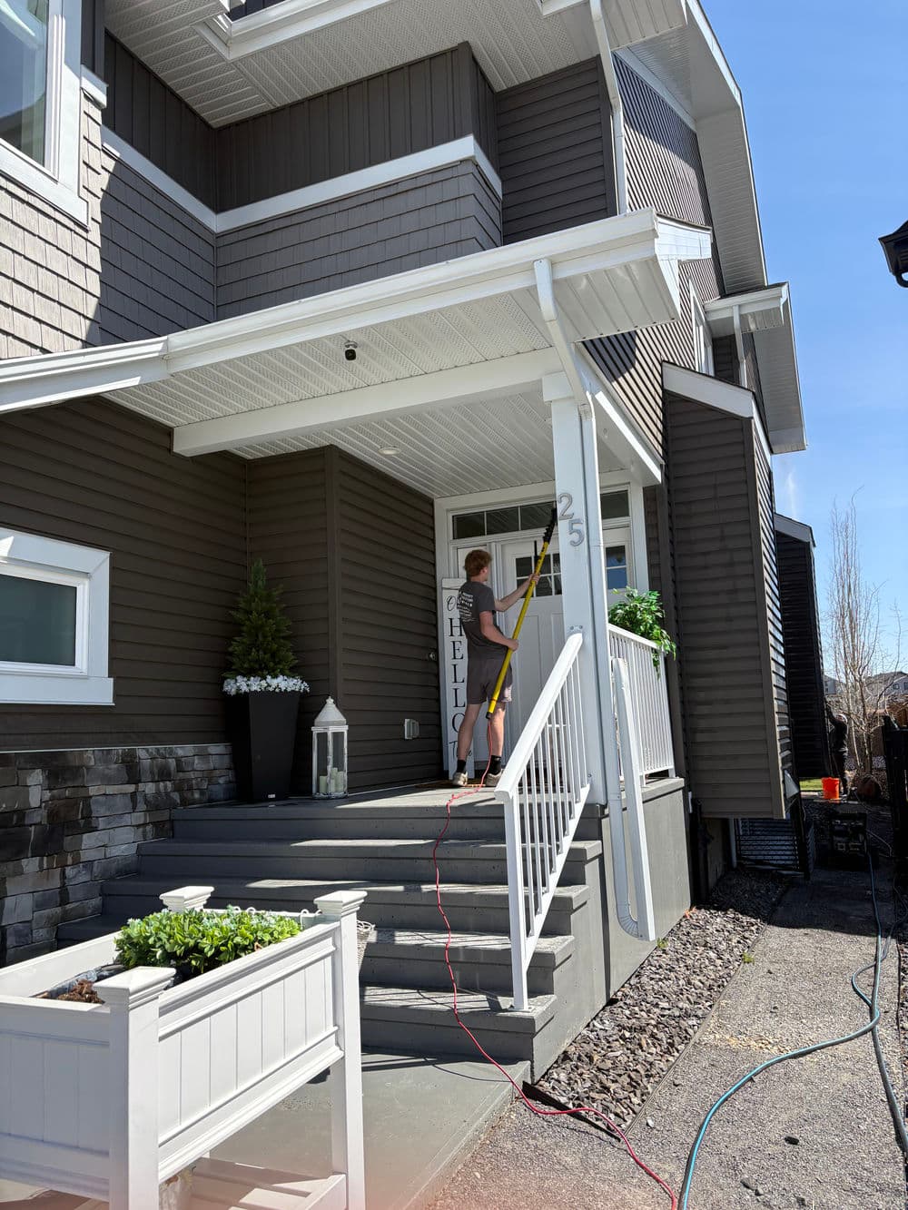 Person cleaning the entrance of a modern home with gray siding and green plants.