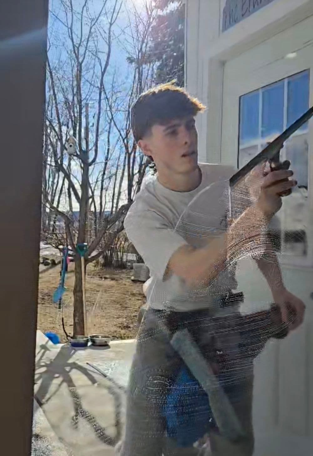 Young man applying adhesive on a door frame in bright outdoor setting, focusing on his task.