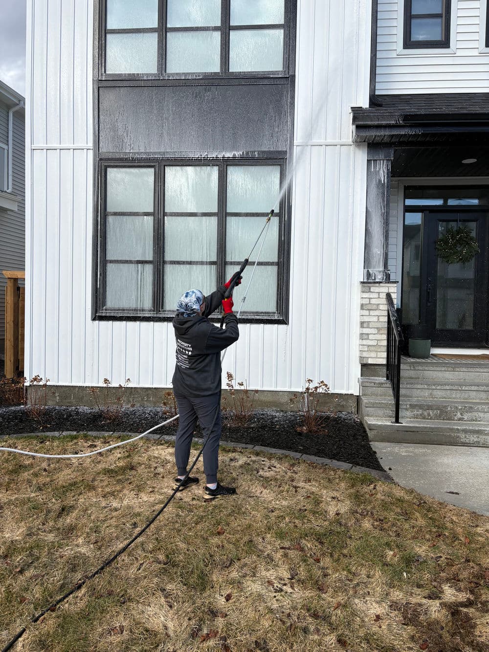Person using a pressure washer to clean the exterior of a modern home with large windows.