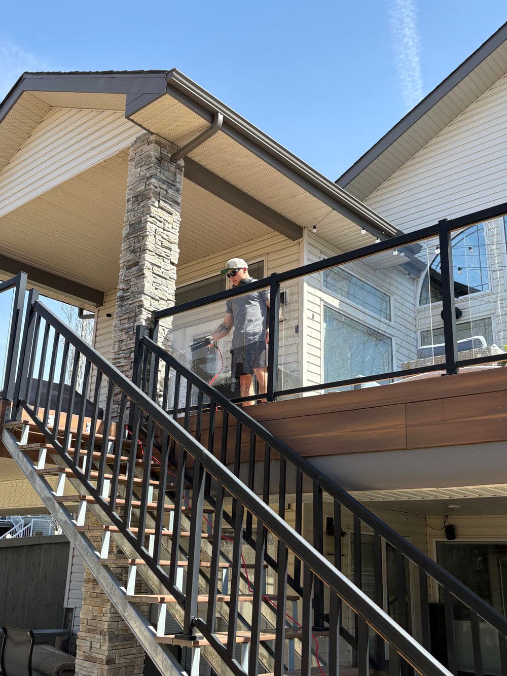 Man cleaning a glass railing on a modern deck of a stylish home.