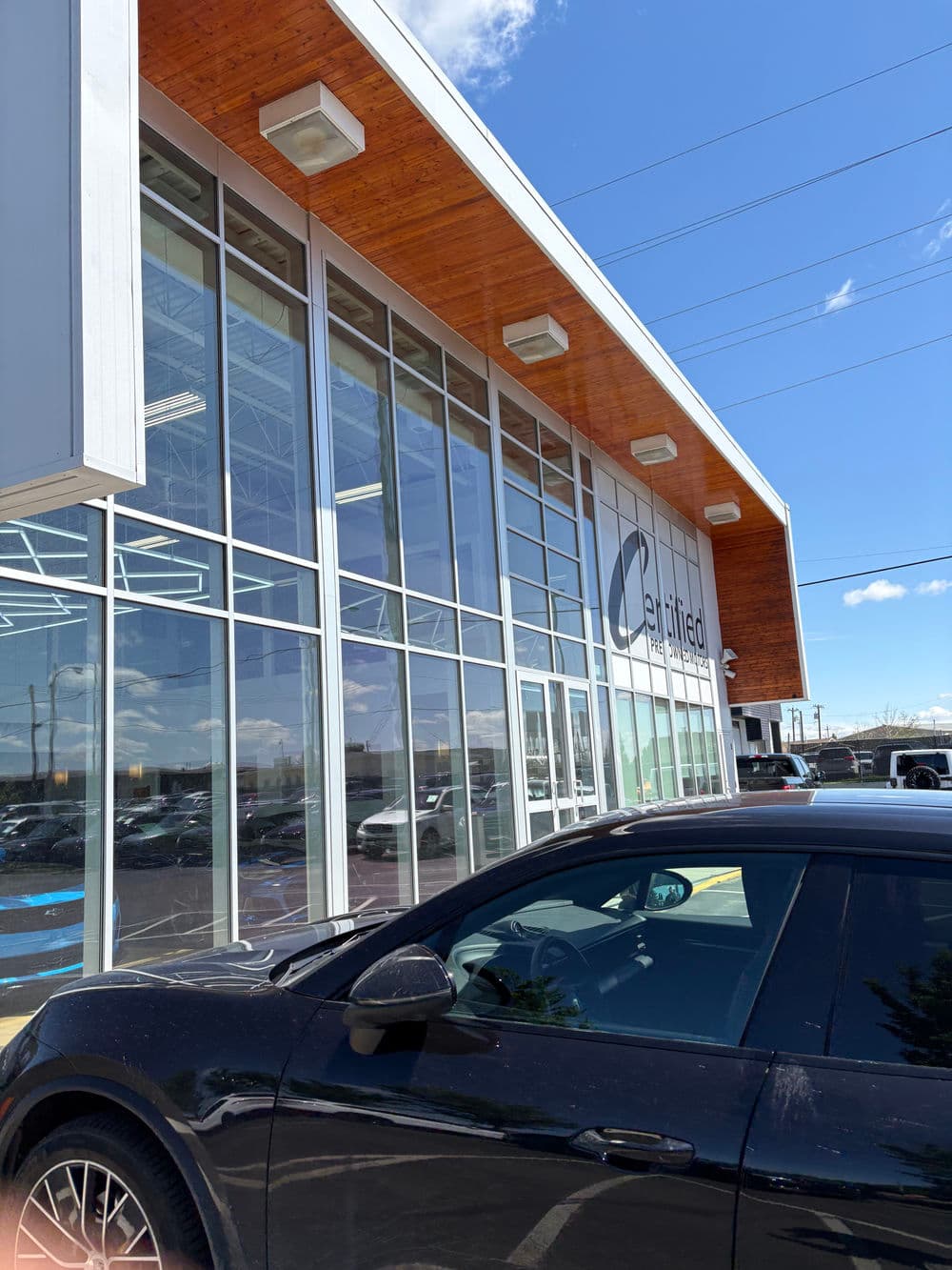 Modern car dealership exterior with large glass windows and a black vehicle in foreground.